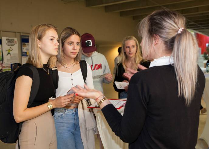 Zwei Studentinnen lassen sich von einer Frau an einem Infostand beraten.