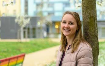 Alexandra lehnt an einem Baum im Park und lächelt in die Kamera.